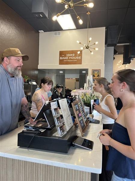 Customers gather at the 1989 Bake House counter as staff assist inside the modern, stylishly lit bakery.