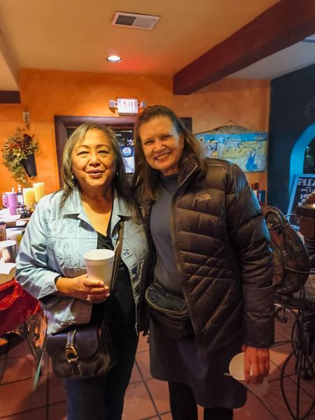 Two women in a restaurant smiling and posing for the photo with drink cups in hand.