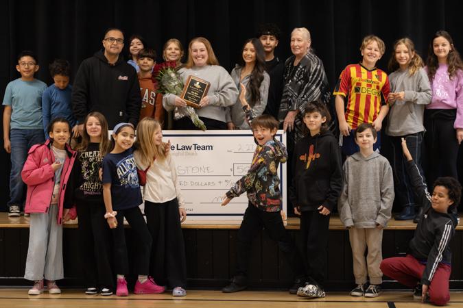Ms. Amy of Acequia Madre Elementary School on a stage with a large check and Teacher Appreciation Award